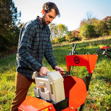 Man operating a tiller in a grassy field with trees in the background