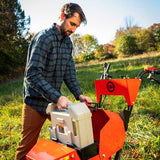 Man operating a tiller in a grassy field with trees in the background